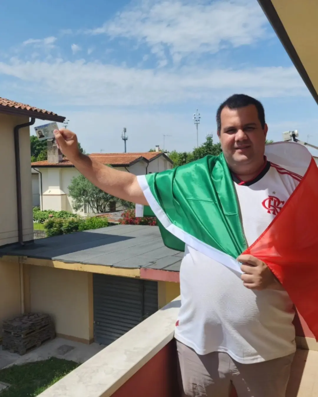 Cliente da Speranza em uma varanda, erguendo o documento de identidade com a bandeira da Itália