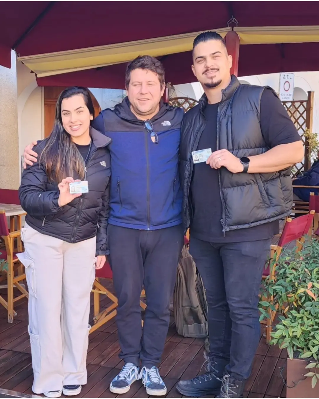 Três clientes da Speranza posando juntos, com os documentos de identidade italianos